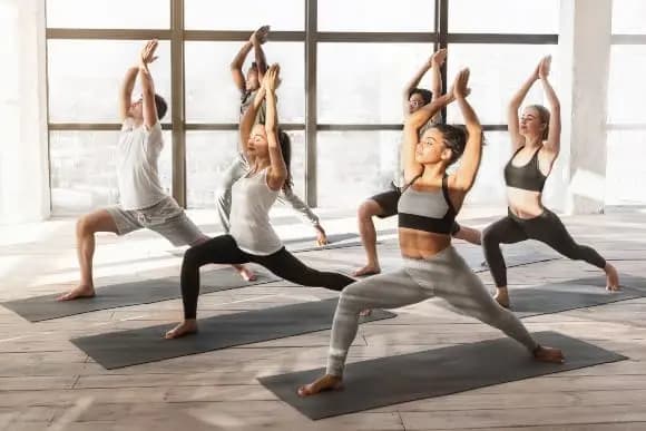 Personen im Yoga Studio führen Warrior 1 Übung auf Yogamatte aus.
