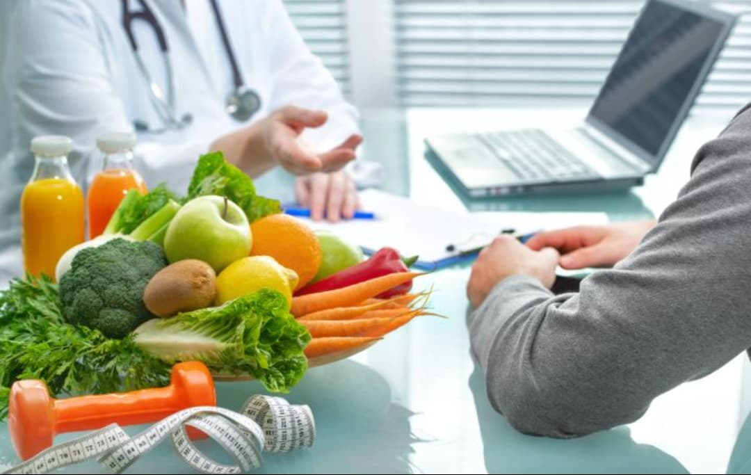 Ernährungsberater und Klient sitzen an einem Tisch, auf dem eine Schüssel mit frischem Gemüse steht