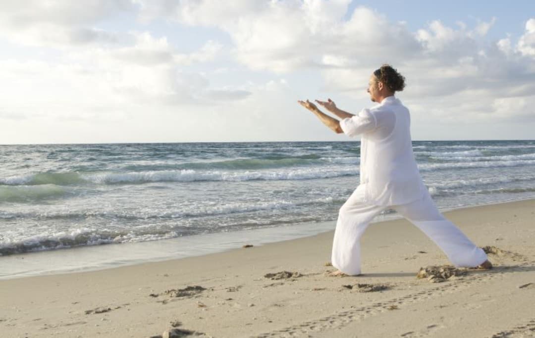 Mann führt am Strand eine Taichi Übung für Anfänger aus