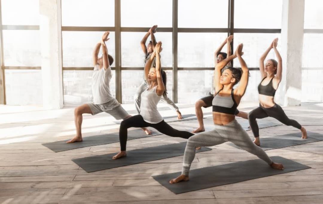 Menschen machen die Crescent Yoga Pose in einem sonnigen Yoga Studio mit vielen Fenstern